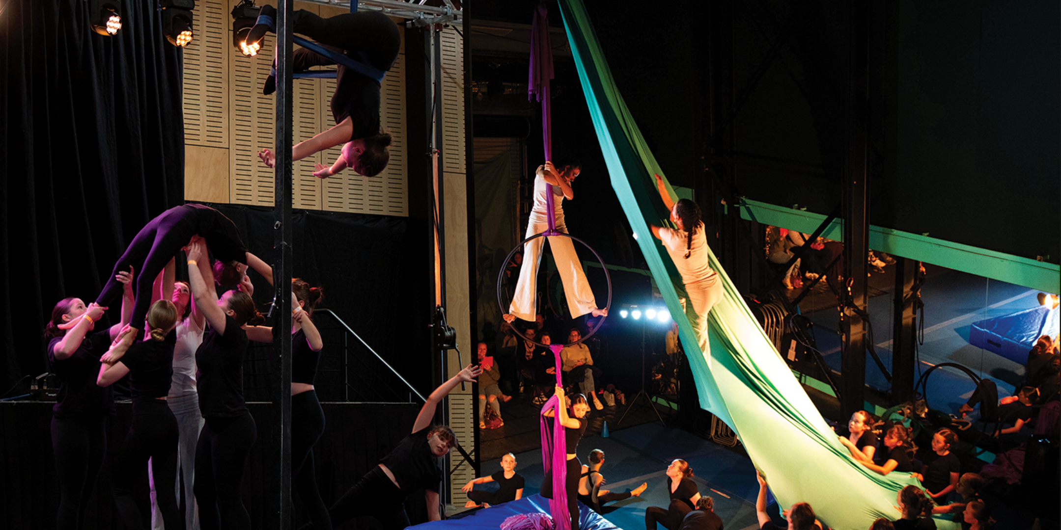 Image of the Unravel show, youth aerialists on Aerial Straps, performing group Acrobatics, Climbing Aerial Silks, and looking down from an Aerial Hoop